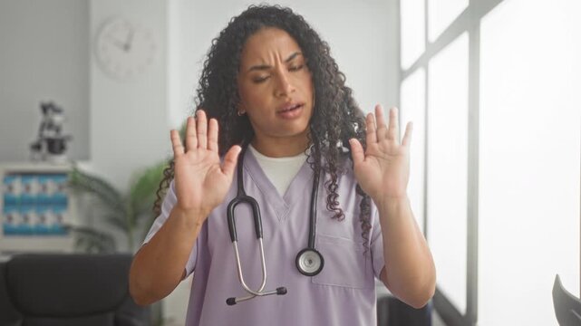 Woman doctor with stethoscope, palms raised in a stop gesture inside a medical building; professional caution concern.