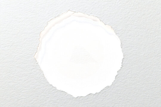 This bright photograph captures a circular hole torn through the center of a piece of textured white paper creating a simple and clean artistic design element