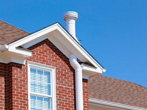 A classic brick house with white trim and gutters against a clear blue sky.