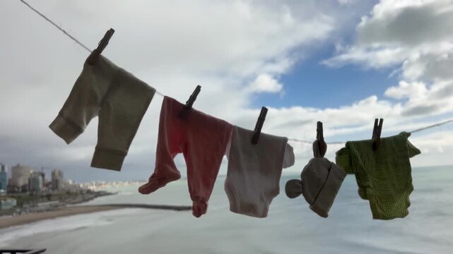 Baby clothing hanging on an outdoor clothesline to air dry naturally, with a coastal city skyline and ocean background. Concept of urban green living, energy-saving , and sustainable family living. 