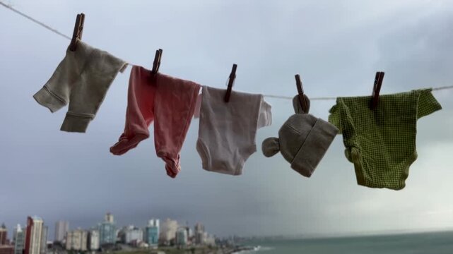 Baby clothing hanging on an outdoor clothesline to air dry naturally, with a coastal city skyline and ocean background. Concept of urban green living, energy-saving , and sustainable family living. 