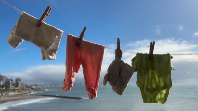 Baby clothing hanging on an outdoor clothesline to air dry naturally, with a coastal city skyline and ocean background. Concept of urban green living, energy-saving , and sustainable family living. 