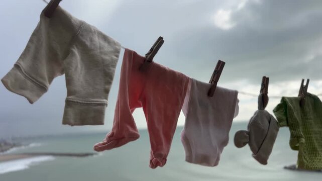 Baby clothing hanging on an outdoor clothesline to air dry naturally, with a coastal city skyline and ocean background. Concept of urban green living, energy-saving , and sustainable family living. 