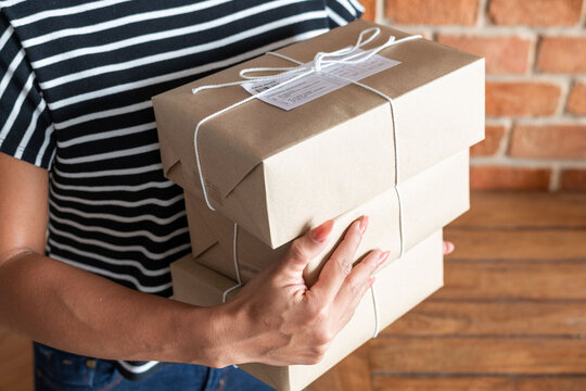 Person holding two brown packages tied with white string indoors.