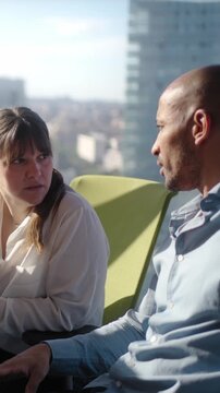 Vertical. Male and female colleagues having a serious conversation in a sunlit modern office. Corporate scene conveying disagreement, concern, negotiation and professional problem solving.