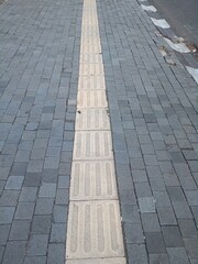 Obraz premium Straight row of tactile paving tiles on paved sidewalk, guiding path for visually impaired pedestrians, urban accessibility facility in Salatiga, Indonesia.