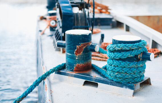 Weathered mooring bollards with blue rope on a boat deck by the water