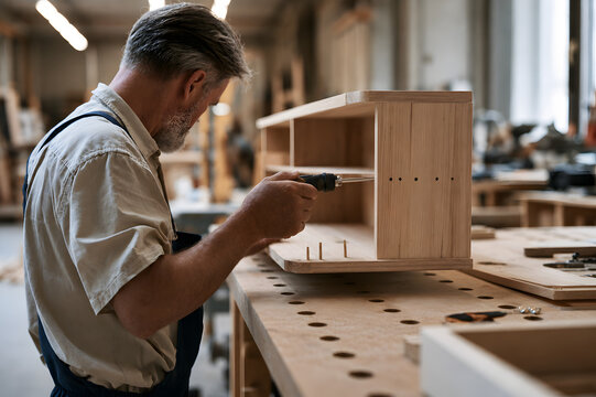 Carpenter Assembling Wooden Cabinet with Screwdriver in Furniture Workshop