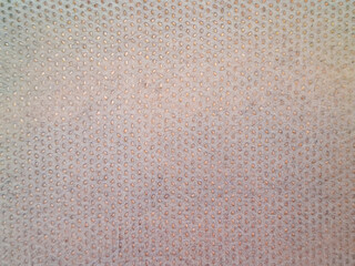 Close-up texture of light beige perforated fabric on car pickup roof lining, breathable mesh material, uniform small holes pattern, automotive interior surface. © Asyraf