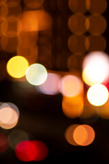 Fototapeta premium Vertical night city bokeh texture with warm glowing building lights and colorful traffic illumination, abstract background.