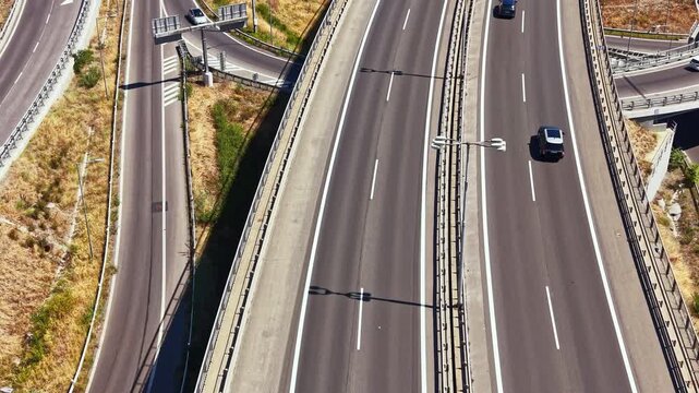 Cars drive along the highway with multiple lanes and pathways. The setting is bright and the scene shows an urban landscape with green areas nearby.