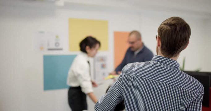 Business team discusses project details in office with woman presenting to businessman and colleague present in background