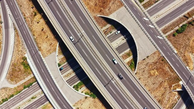Several vehicles travel on a network of highways with multiple lanes and overpasses. The scene shows dry land and surrounding nature. It is a clear day with bright sunlight.