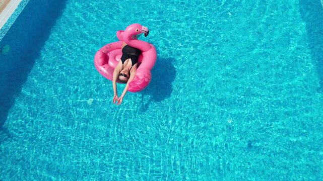Aerial drone view of woman relaxing on flamingo pool float in pool in hotel. Summer holidays, enjoying summer vacations, luxury hotel

