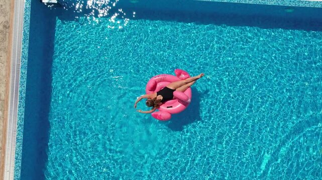 Aerial drone view of woman relaxing on flamingo pool float in pool in hotel. Summer holidays, enjoying summer vacations, luxury hotel
