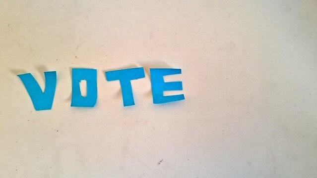 Bright blue paper cutout letters spelling vote on white surface
