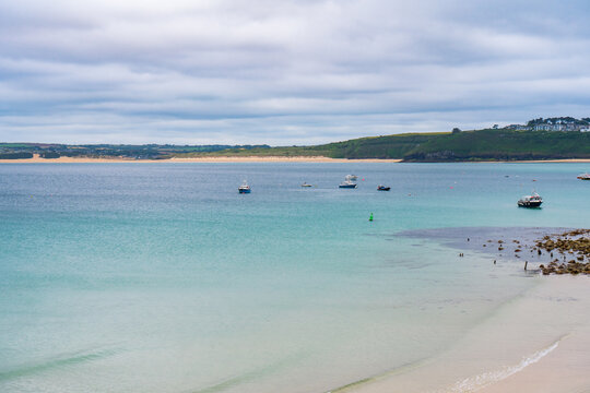 Coastal landscape of calm azure waters and sandy shoreline with anchored boats. Cornwall, UK.