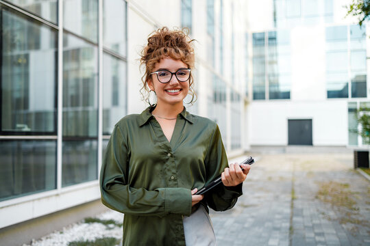 Woman smiles and holds a folder outside a modern building in the city