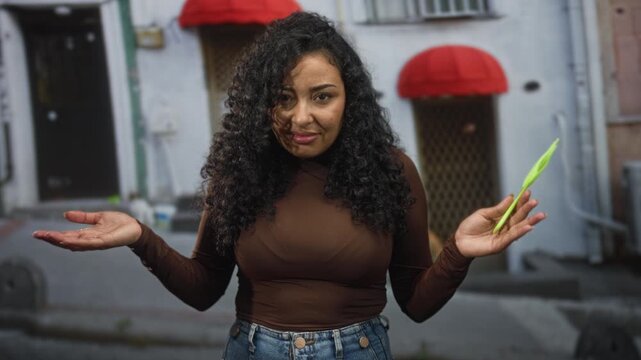 Woman holds green comb in right hand and shrugs with open palms on an urban street storefront; bemusement haircare routine.