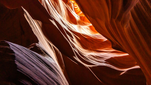 Abstract sandstone formations inside a narrow slot canyon, featuring flowing rock textures, warm red tones, dramatic curves, and sunlight illuminating the natural sculptural landscape.
