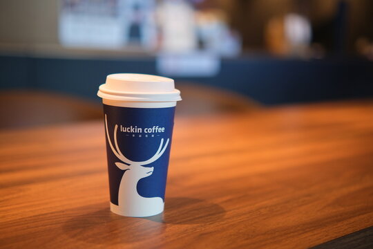 A Luckin Coffee paper cup with a lid and deer logo sitting on&nbsp;table in a cafe in Nanning, China. Luckin Coffee Inc is a Chinese coffee company and coffeehouse chain