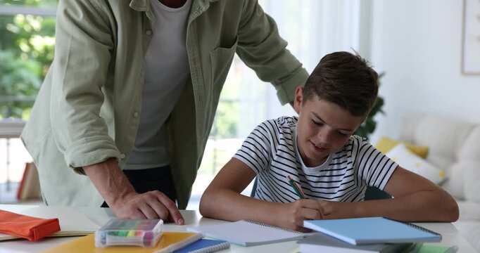 Father helping his son with homework at white table indoors, closeup