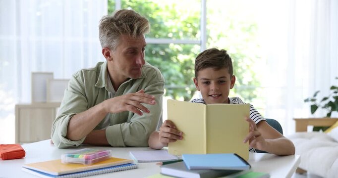 Father helping his son with homework at white table indoors