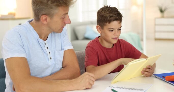 Father helping his son with homework at white table indoors