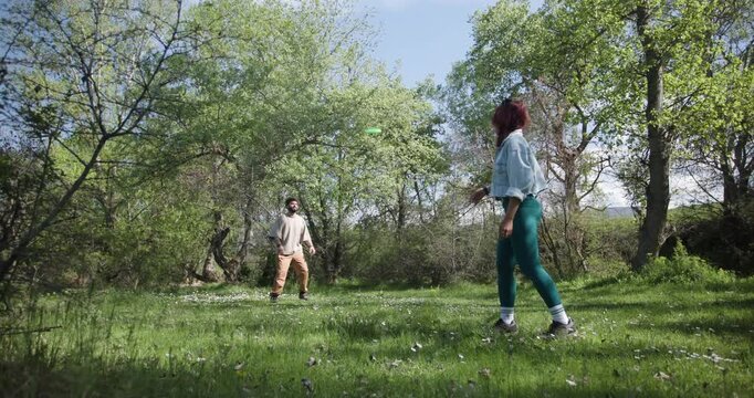 Couple Playing Frisbee in a Sunny Park Surrounded by Trees