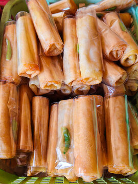 Fried spring rolls packaged in clear plastic wrap piled in a green basket at a street food market