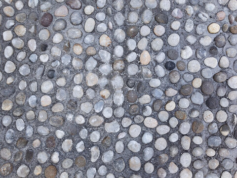 Pebble mosaic surface texture close-up, smooth river stones set in grey cement for outdoor paving
