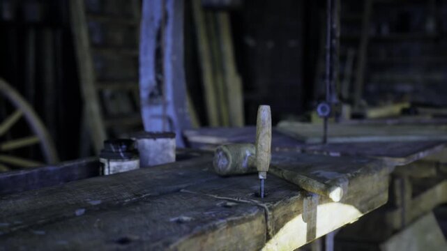Dusty wooden workbench with drill bit, dimly lit vintage workshop, scattered tools and wood shavings on worn plank, metal clamp embedded in bench, blurred