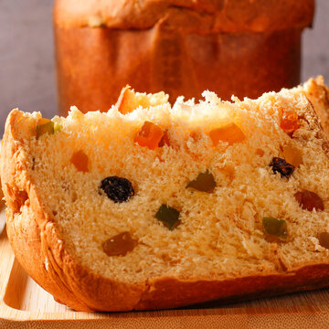 A slice of traditional Christmas panettone, showing its soft, fluffy crumb, candied fruit, and raisins, on a bamboo tray
