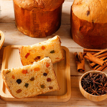 Slices of Christmas panettone with candied fruit, accompanied by dried orange, cinnamon, and star anise on a rustic table