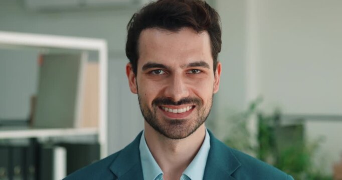 Portrait of Hispanic businessman smiles in bright office as shows warm confident expression. Businessman turns head directly during calm corporate pose