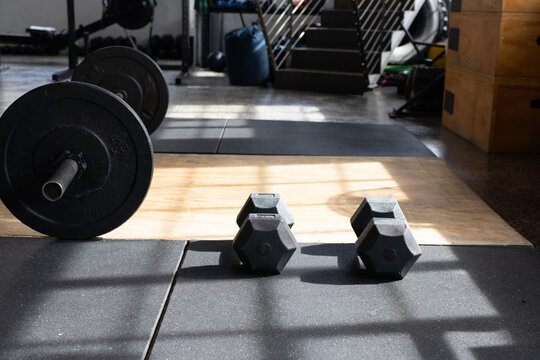 Pair of black hex dumbbells are resting on black mat on wooden lifting platform casting shadows