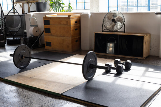 Loaded barbell resting on wood lift platform and rubber mats at gym, sun casting strong shadows