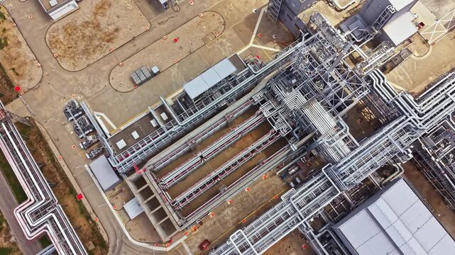 Aerial view of an industrial site shows many pipes, storage tanks, and buildings arranged in a systematic manner. The scene captures the large scale of industrial operations taking place.