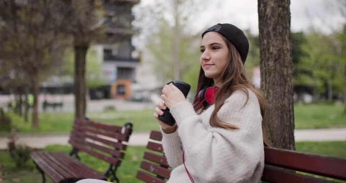 Teen Girl Enjoys Music on Headphones While Relaxing on Park Bench in Urban Setting