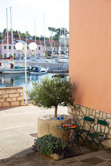 Fototapeta premium Outdoor mediterranean breakfast setup with olive tree in pot, coffee, croissants, and orange juice on a bistro table overlooking Sali marina in Croatia.