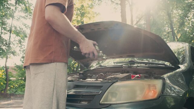 Driver opening car hood during emergency roadside repair on sunny summer day. Repair wrench set is visible in his hands as he prepares simple vehicle inspection.