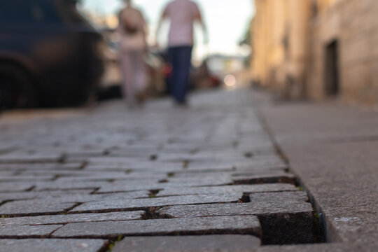 Close-up of wet granite cobblestones laid in rows with people walking in the background