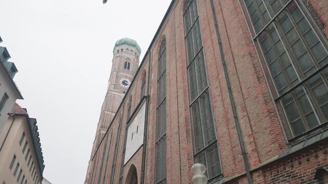 Frauenkirche tower rising above brick facade in Munich alley