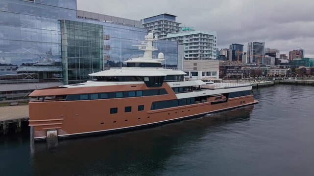 An aerial view captures the stunning La Datcha, an elegant yacht docked in the vibrant heart of Halifax, Nova Scotia, showcasing its impressive design against a picturesque skyline