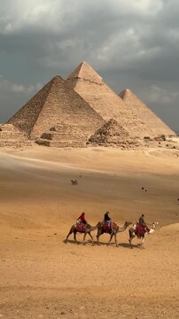 Tourists riding camels in the desert sand in front of the Great Pyramids of Giza in Cairo Egypt