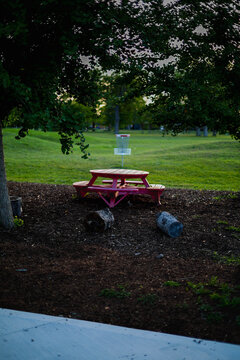 Red picnic table near a disc golf basket at dusk