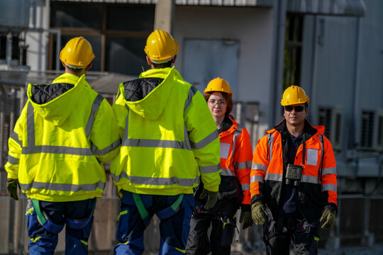 Engineers in glowing yellow jackets carry the last cases out of the switchyard through the substation compound in low golden sunlight at a renewable energy site in Thailand.