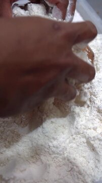 Vertical close up of hands coating raw chicken pieces in white flour, preparing crispy fried chicken