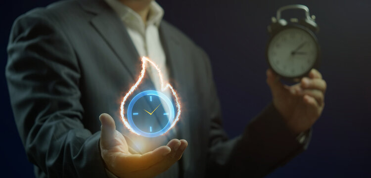 Businessman holding vintage alarm clock while open hand supporting glowing clock icon surrounded by fire flame. Urgent project deadline pressure, time management crisis, and fast speed concept.