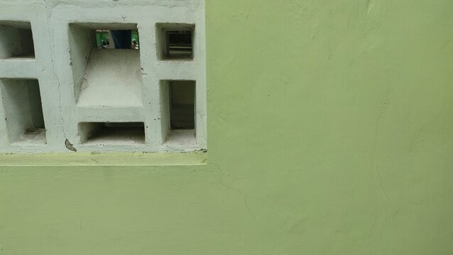 Close-up of a light green painted wall combined with a white concrete ventilation block. Concept of modern architecture, home ventilation, construction materials, and aesthetic background.